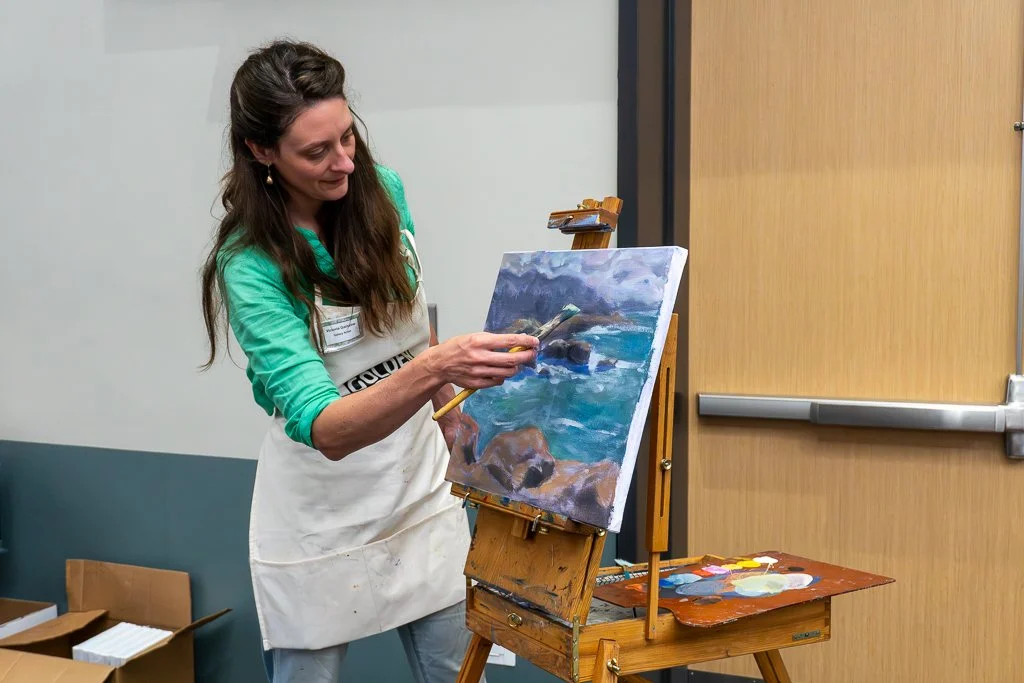 A woman leaning over a canvas, painting a seascape