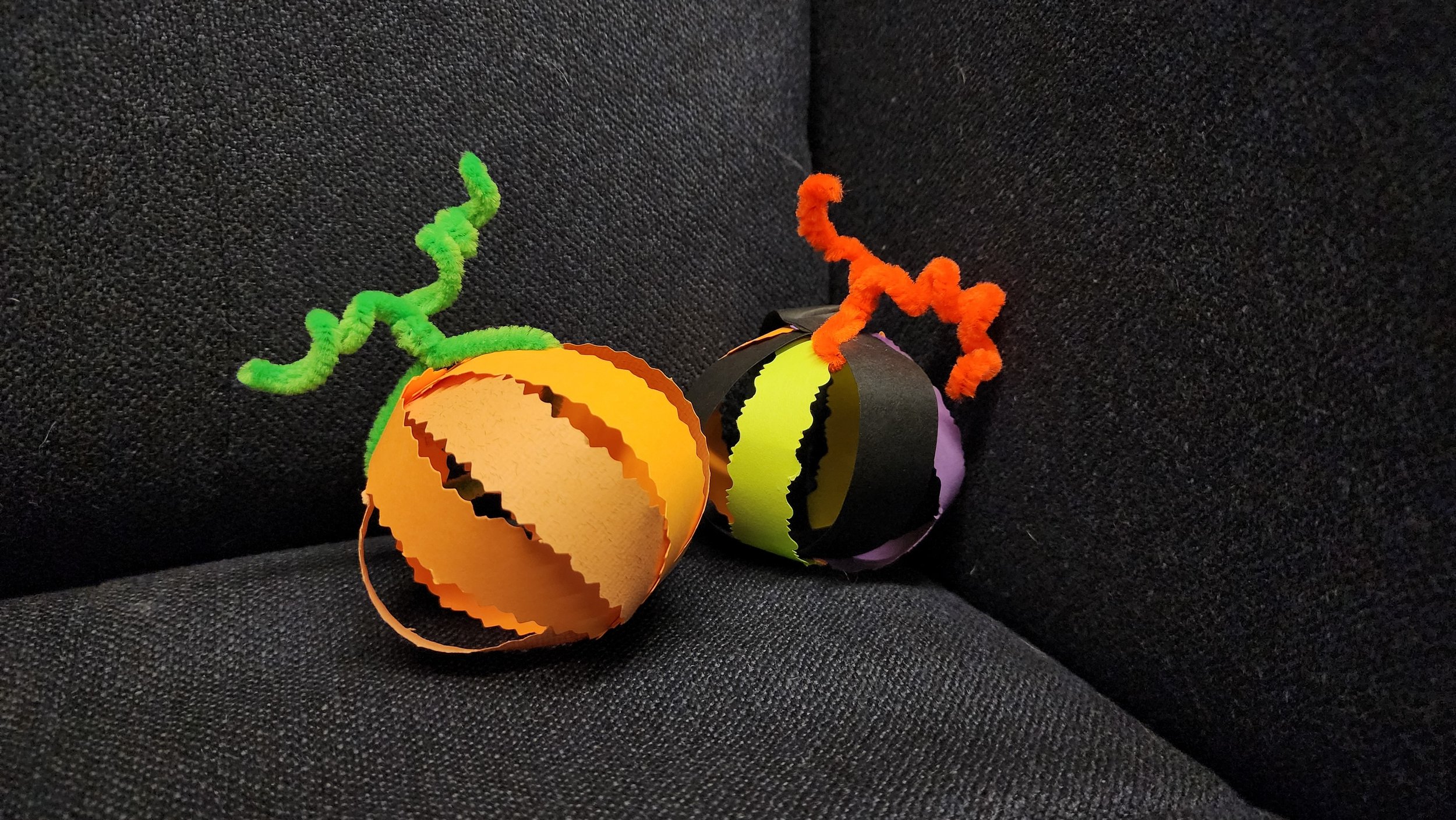 Two paper pumpkins, made from strips of paper attached with a pipe cleaner stem