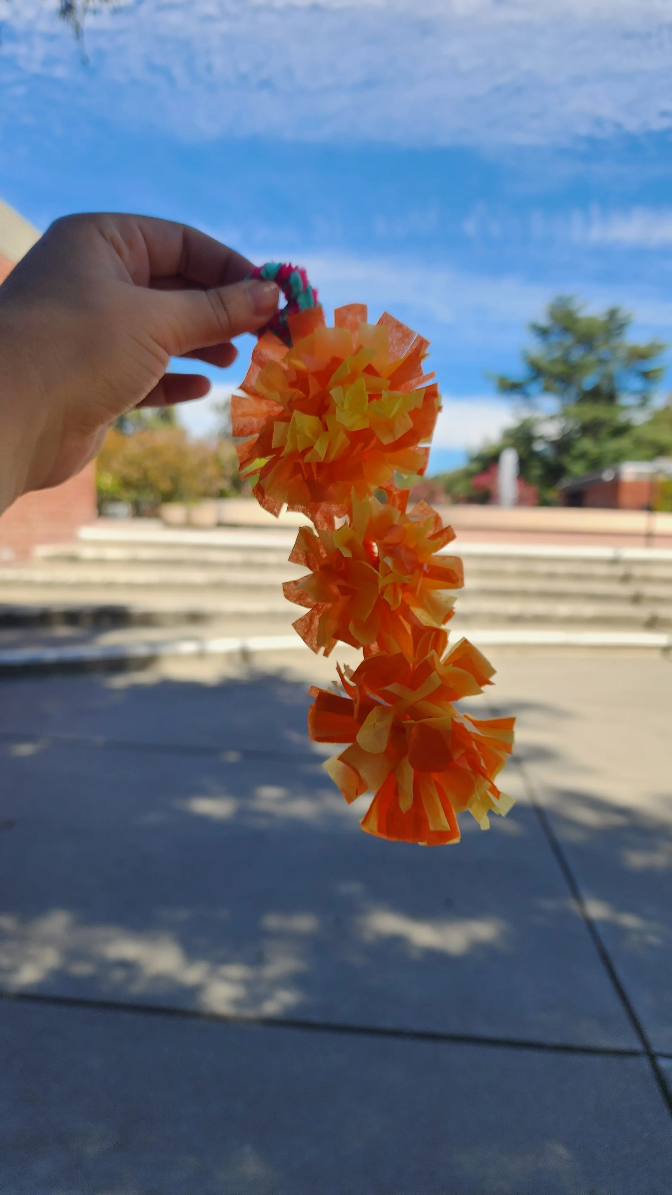 A hand holding a chain of paper marigolds, made from strips of tissue paper.