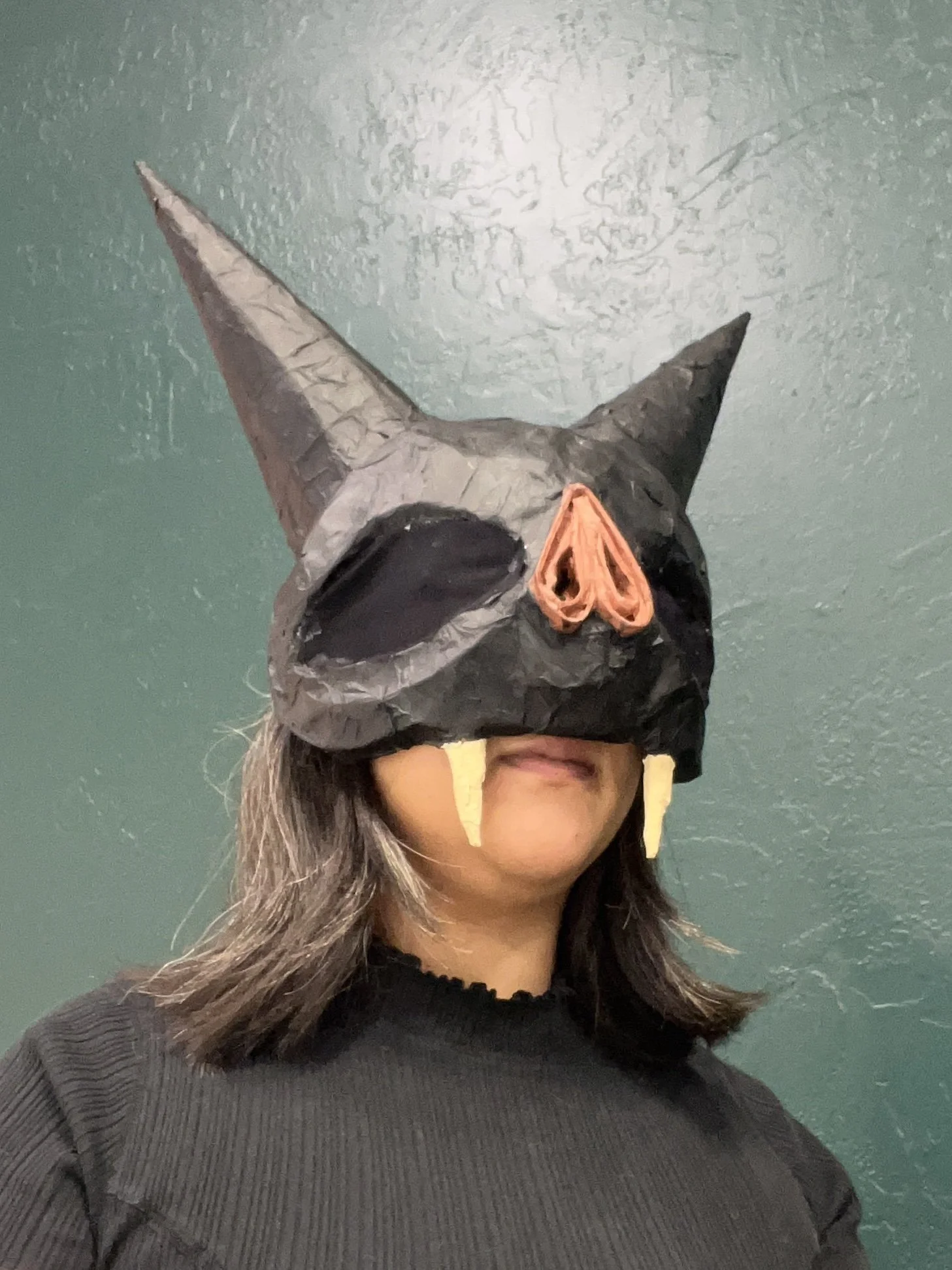 A woman wearing a papier-mâché bat mask that covers the top of their head. Fangs extended past the mask.