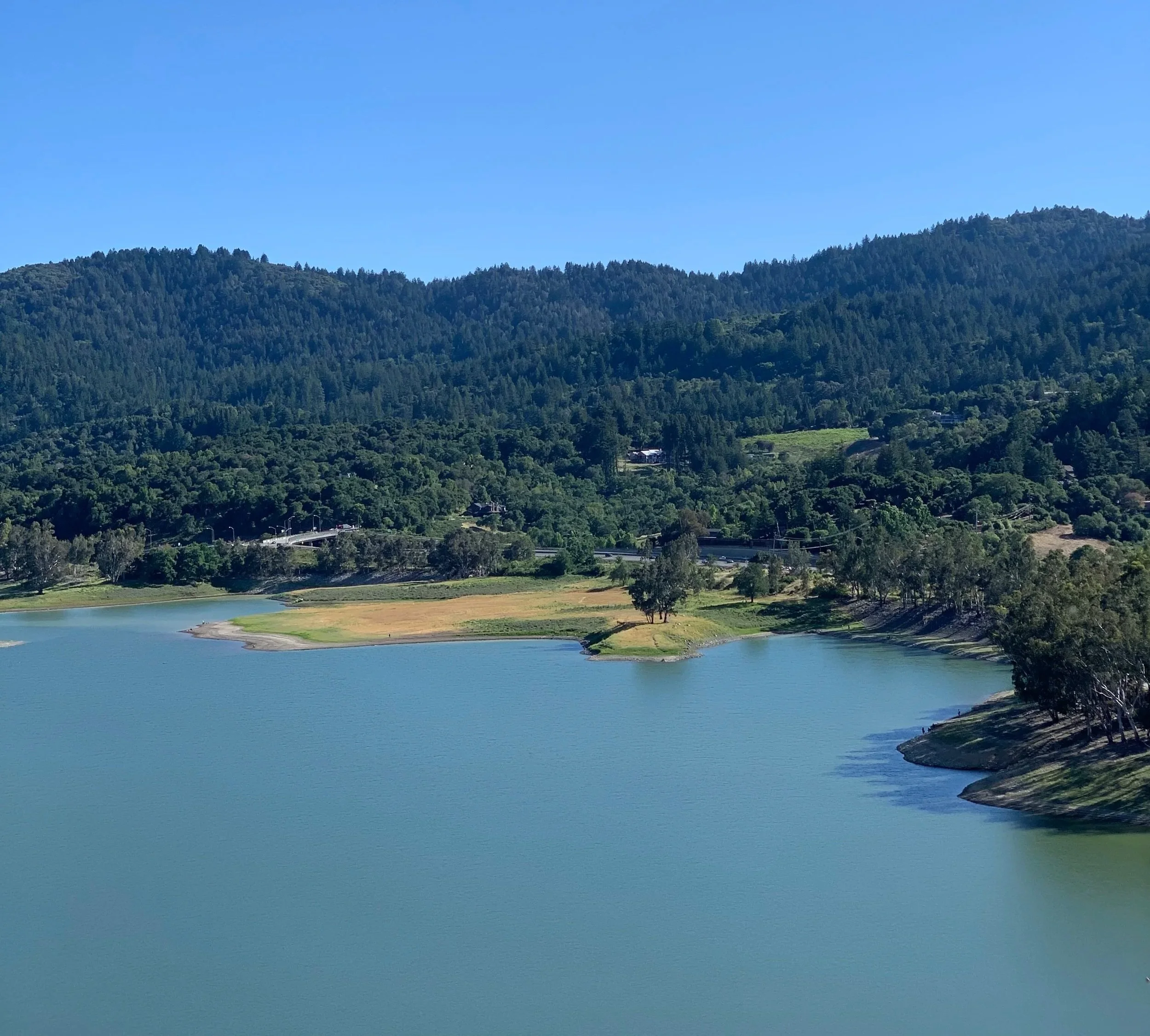 An arial photo of a blue body of water surrounded by forested hills