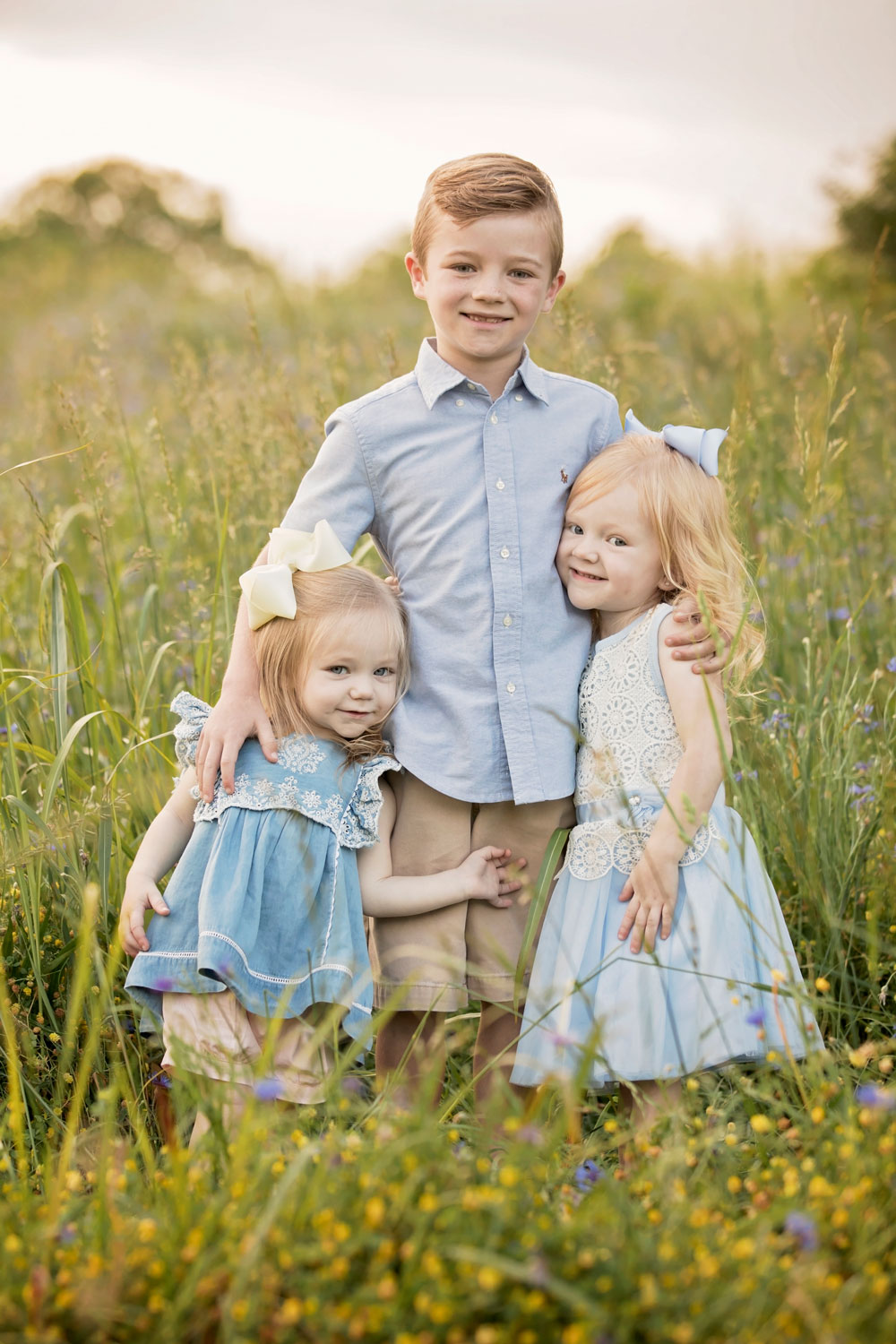 Three siblings posing in grassy field. 