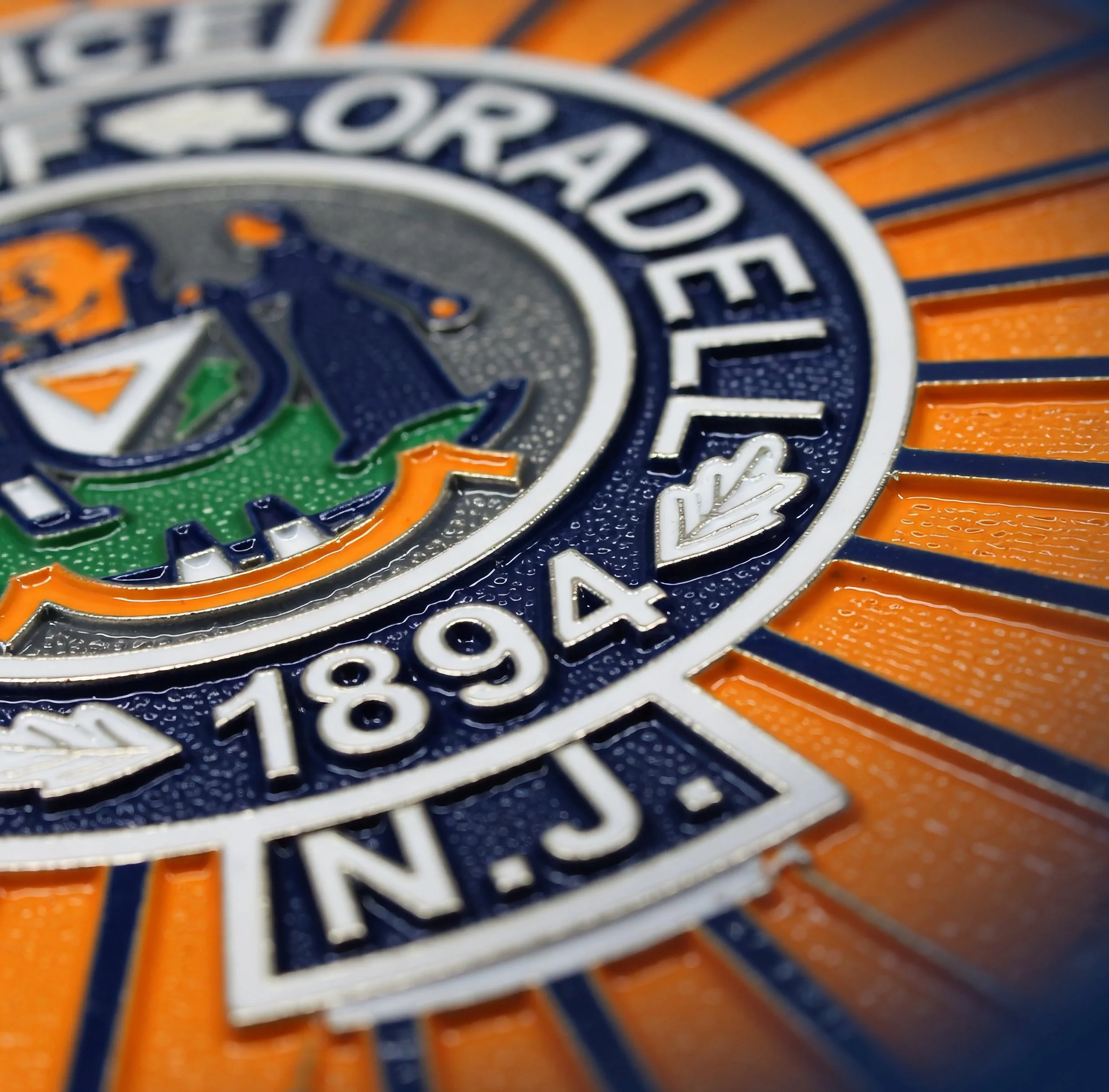 Close-up of the Oradell badge with water droplets on it and orange and blue background.