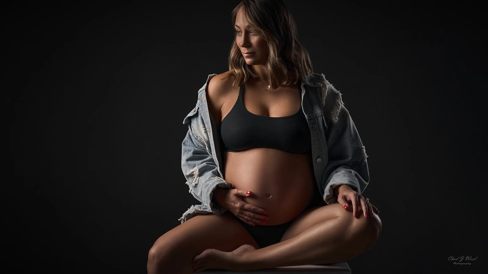 Mesa Pregnancy Glamour Photography: Studio photo of a pregnant woman sitting on a box in a jean jacket