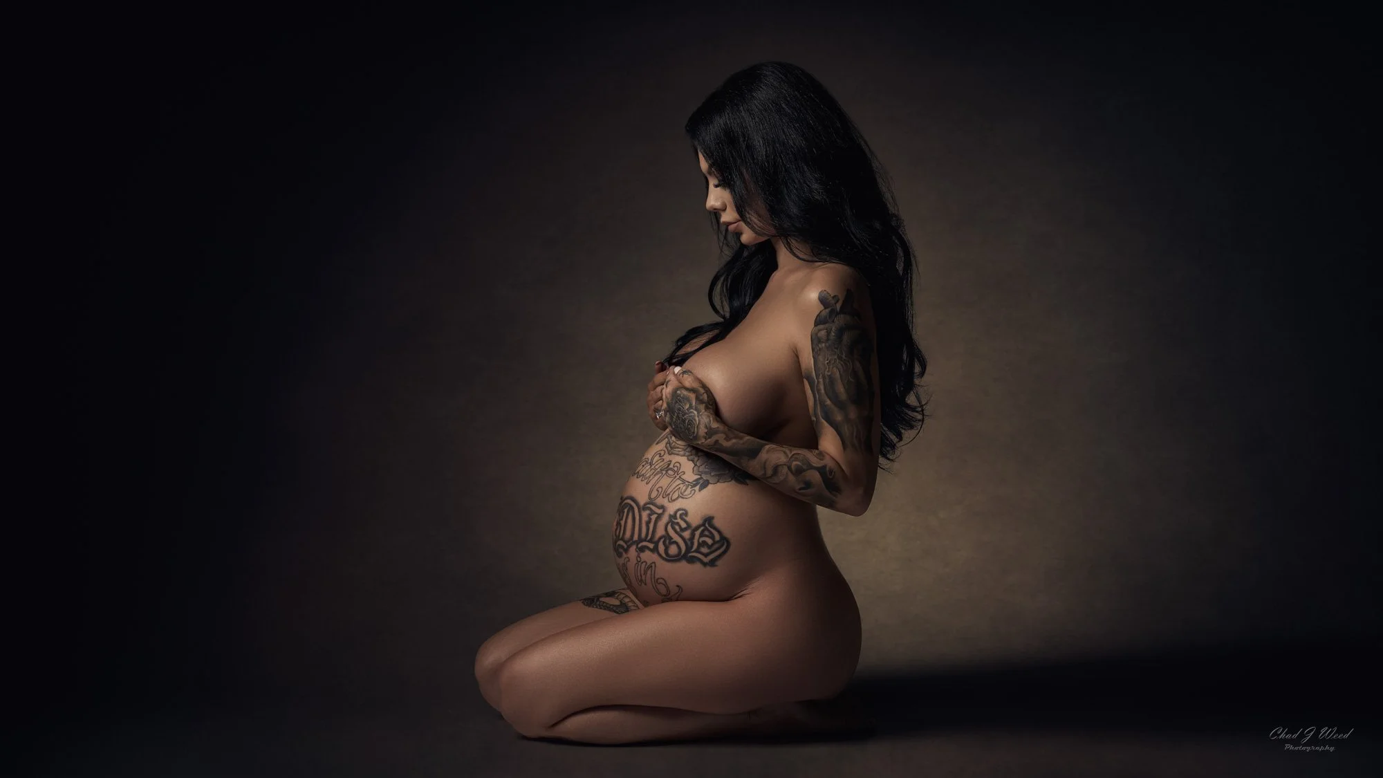 Maternity boudoir photographer image with tattoos visible while kneeling