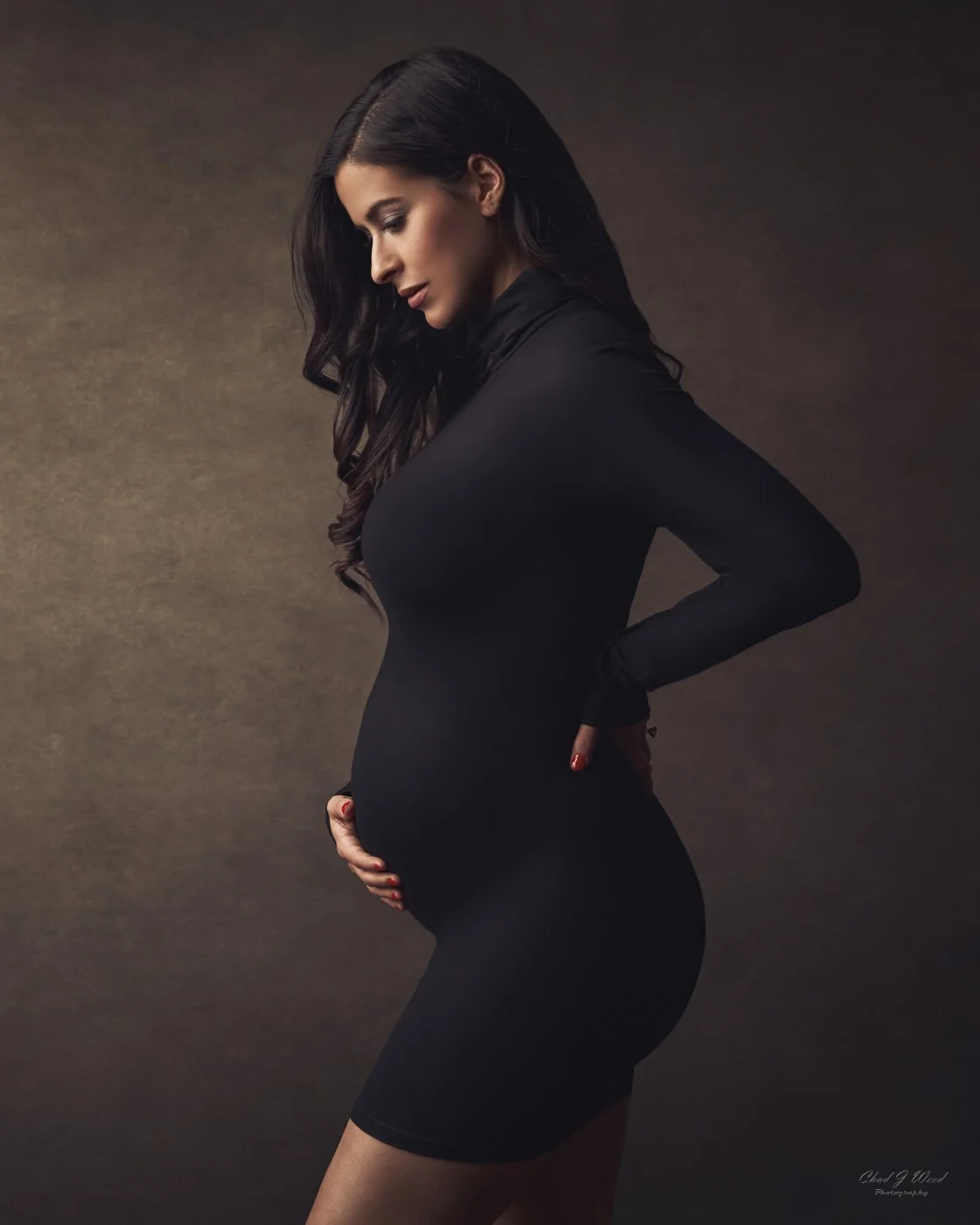 Pregnant woman in black dress and dramatic lighting for fine art maternity session portrait