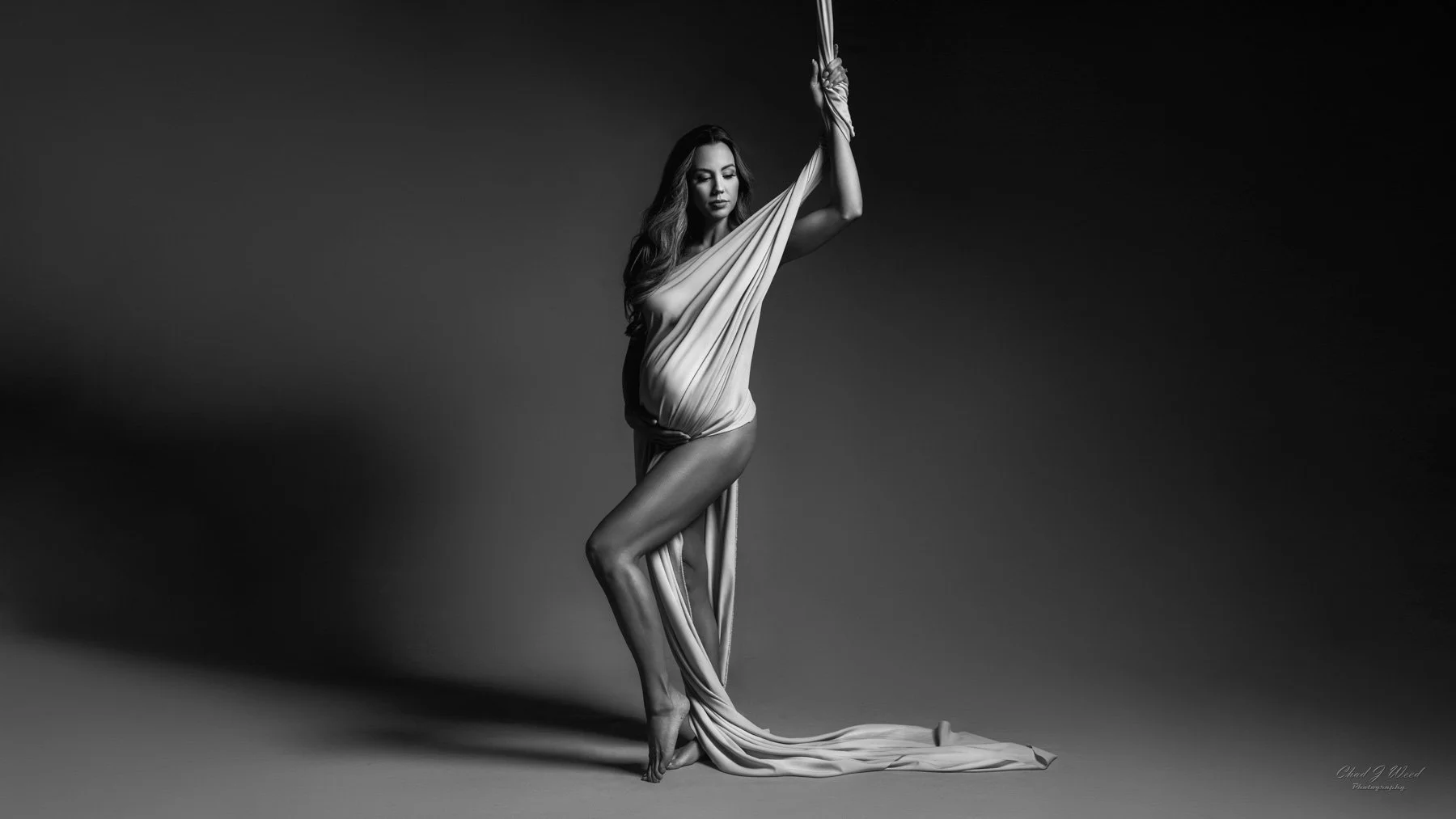 Fine art maternity photoshoot of pregnant woman wrapped in soft material with dramatic light glow