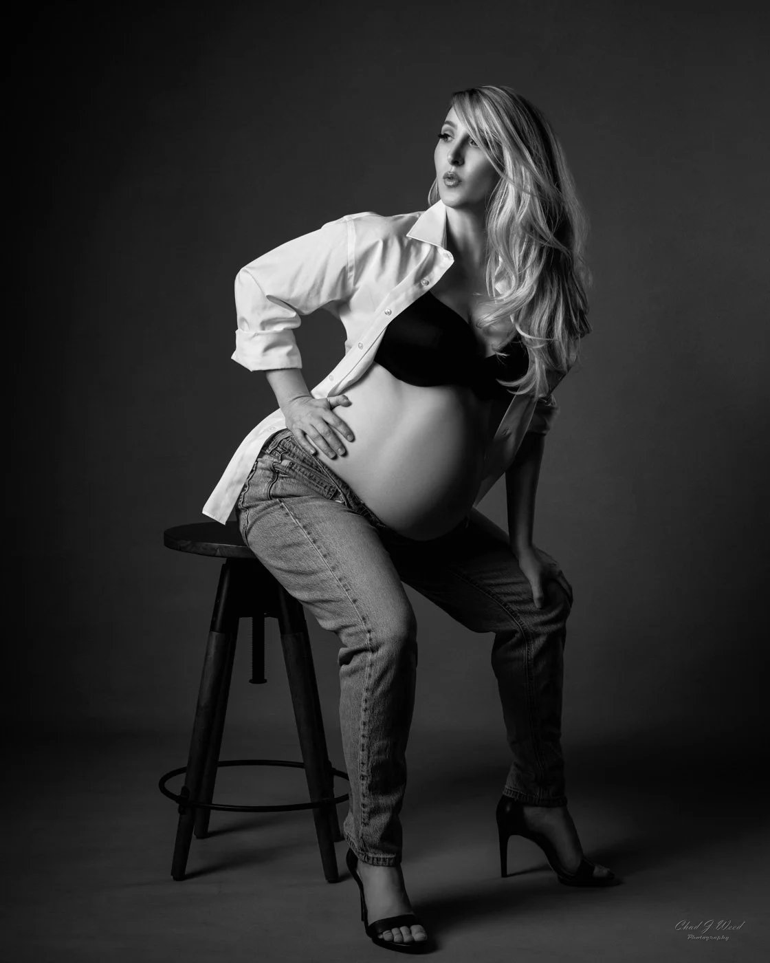 Maternity Photoshoot Jeans: Fashion maternity photo in jeans and white shirt sitting on a stool with high heels