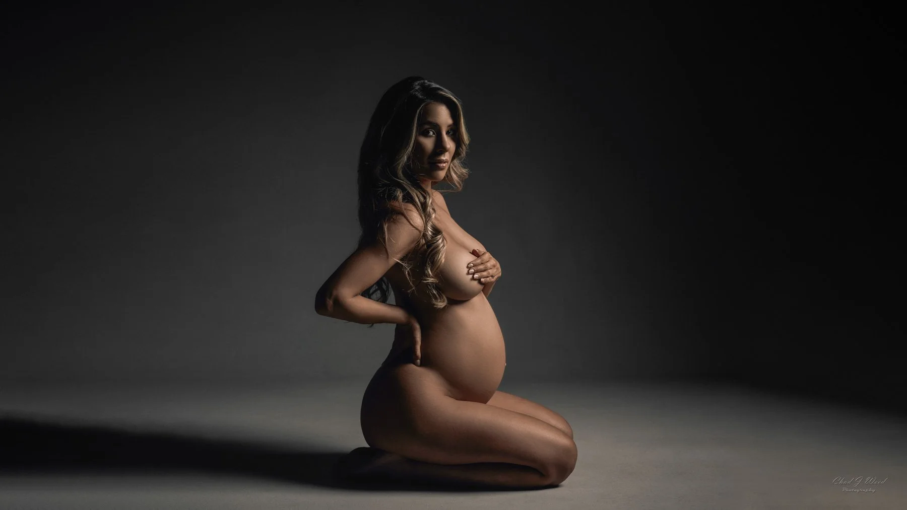Fine art maternity photoshoot with kneeling pose in dramatic lighting
