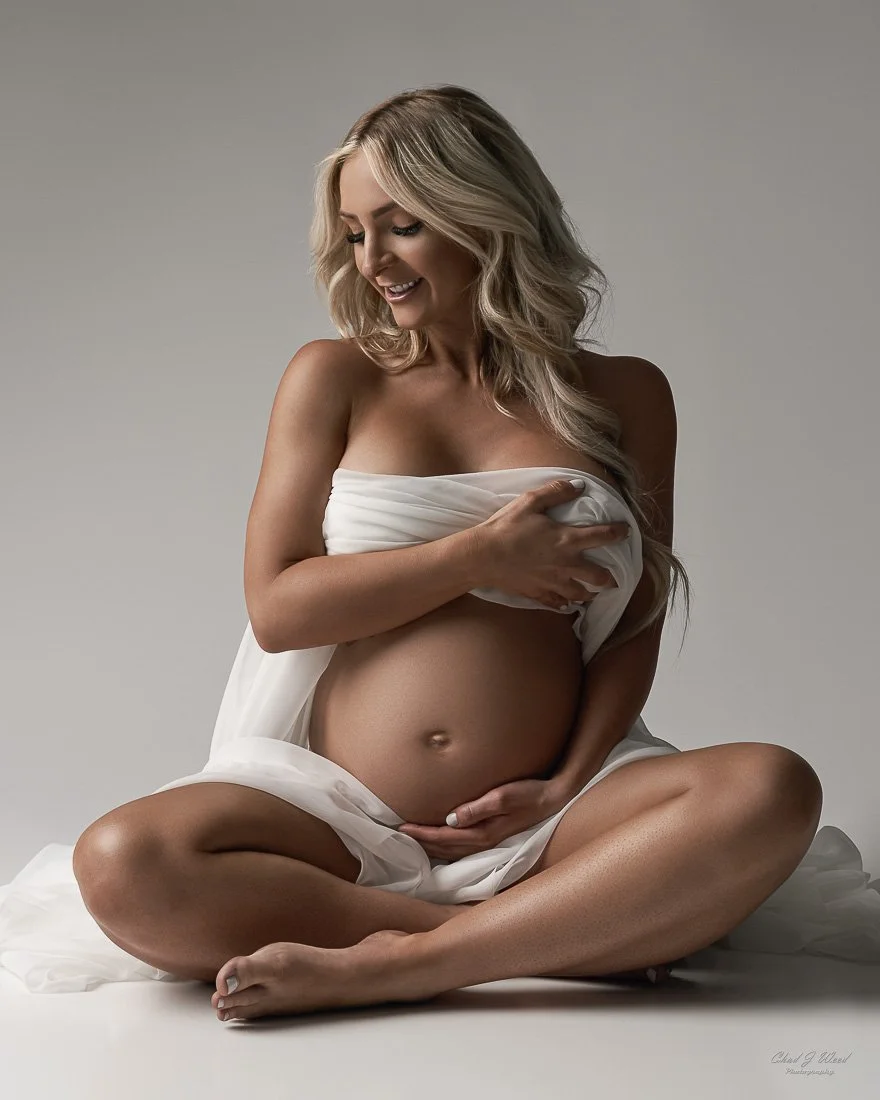 Maternity Photographer Phoenix: Expectant mother sitting on the floor with legs crossed and smiling