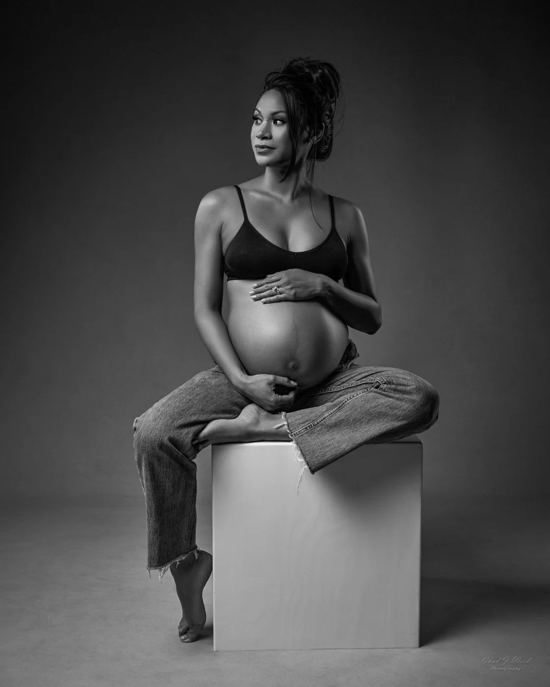 Sitting on box in jeans with hands on belly maternity photography pose