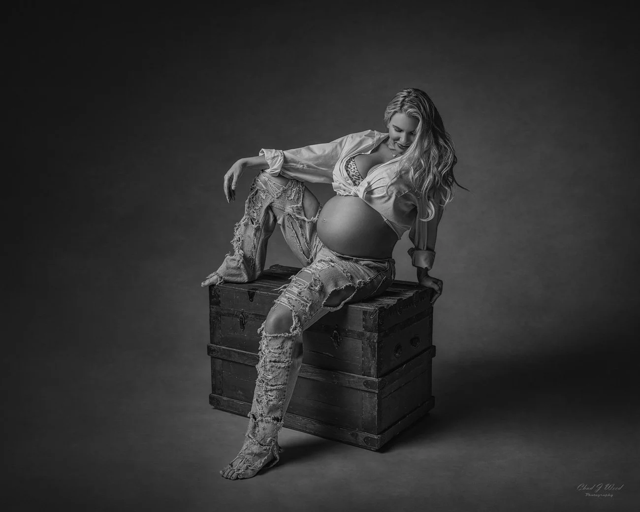 Phoenix Maternity Photography: Pregnant woman sitting on a vintage box with a glowing smile wearing torn jeans