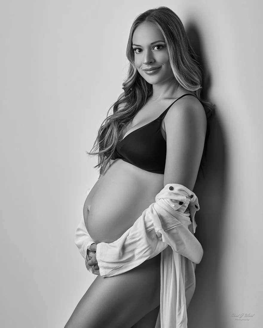 Beautiful Pregnant woman wearing lingerie and a white shirt in intimate maternity photography pose against the wall