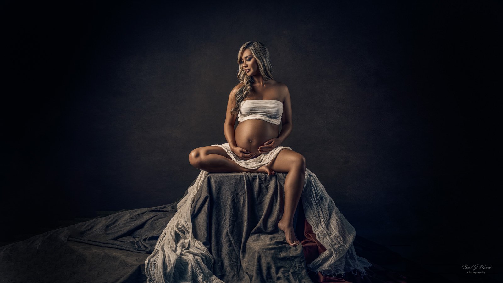 Pregnancy Photography Phoenix: Pregnant woman sitting on a box with hands on her belly
