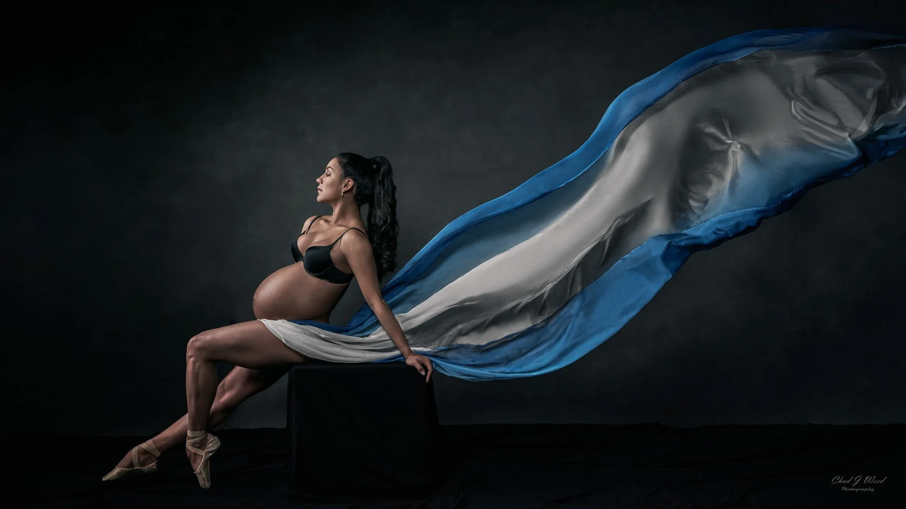 Sitting with leg extended maternity pose on a box with dramatic flowing material