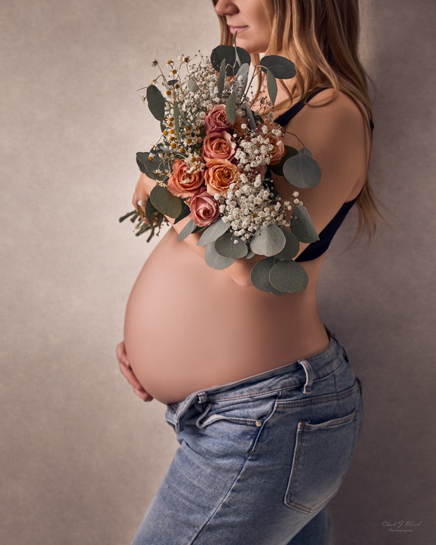 Close-up of baby bump in unbuttoned jeans holding flowers