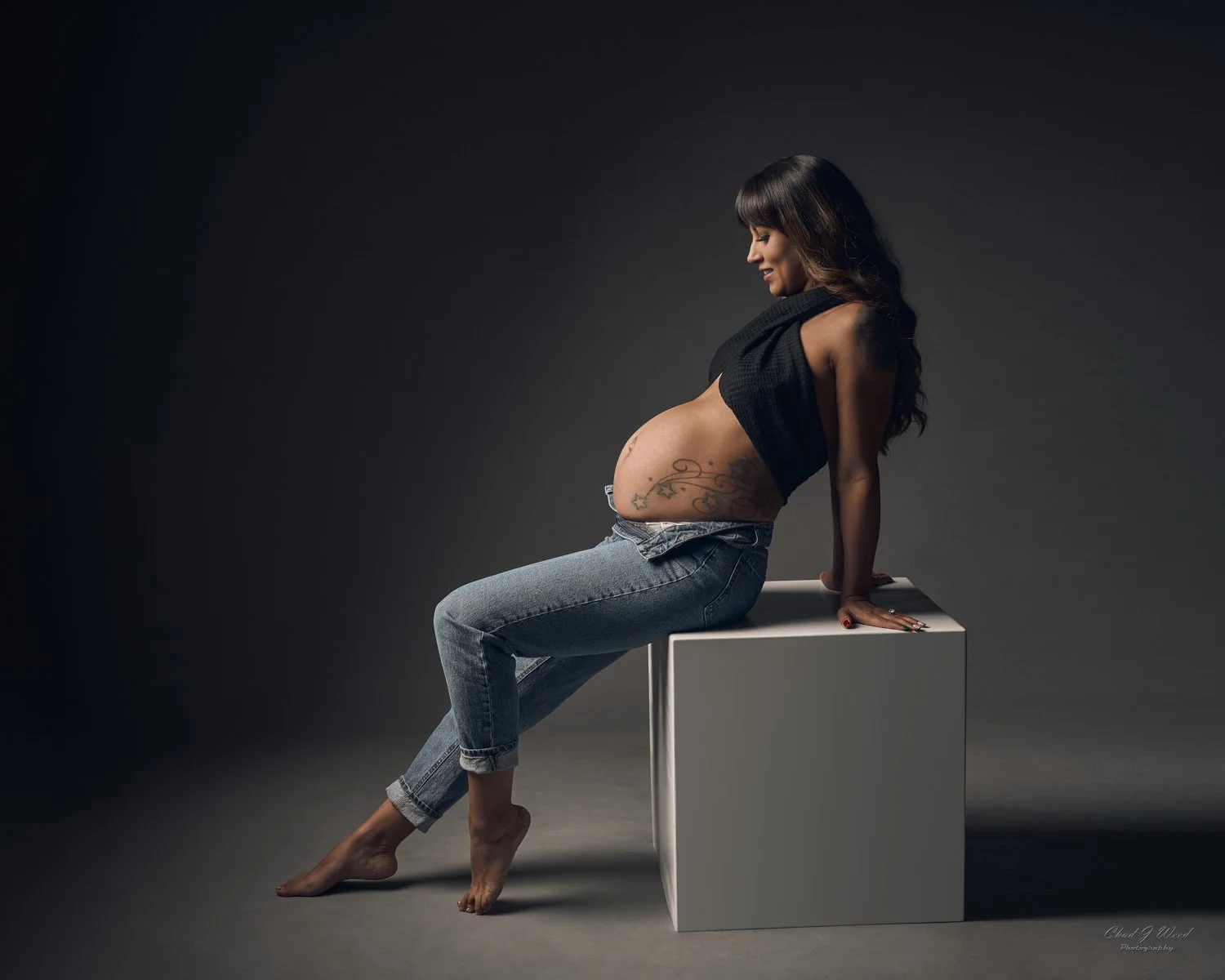 Pregnancy Photographer Phoenix: Pregnant woman in jeans sitting on a box in soft lighting