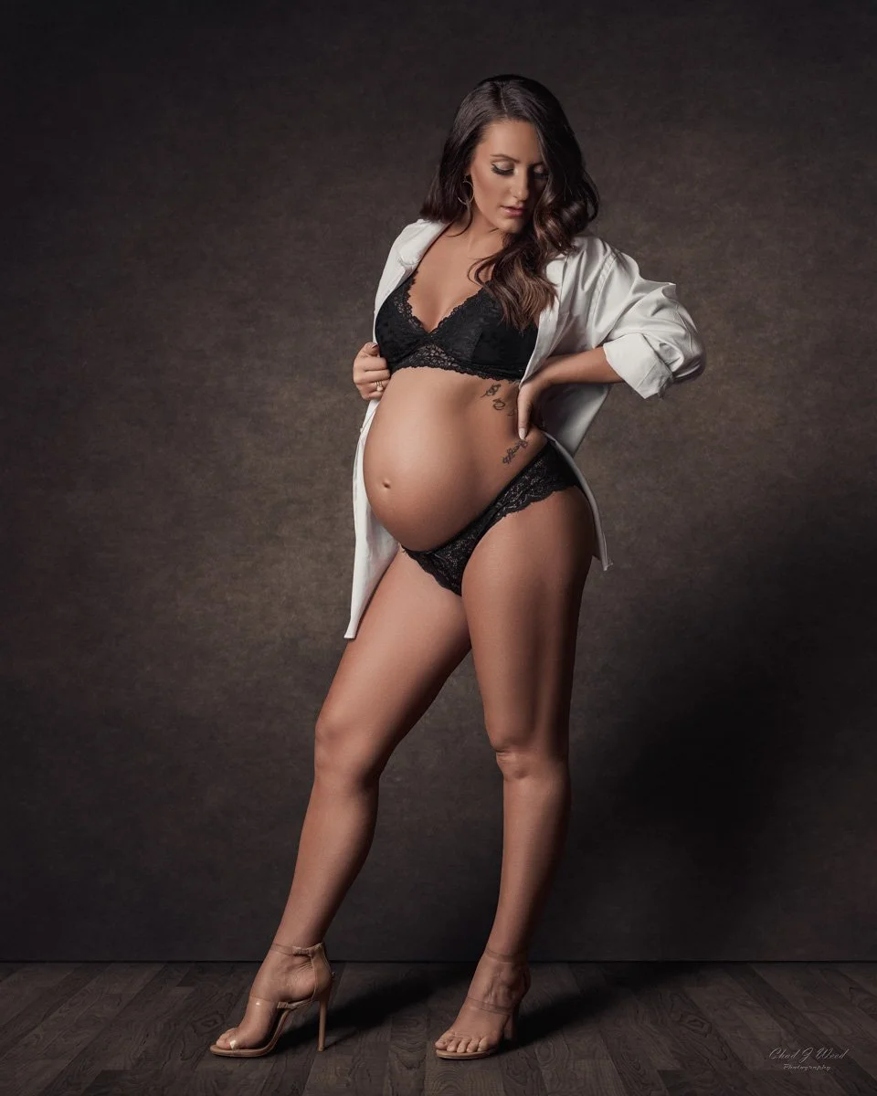 Pregnant woman standing in heels and a white button up shirt during a maternity photography studio shoot
