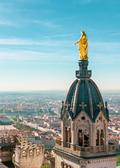 Statue of the Virgin Mary on top of a church dome, overlooking a cityscape.