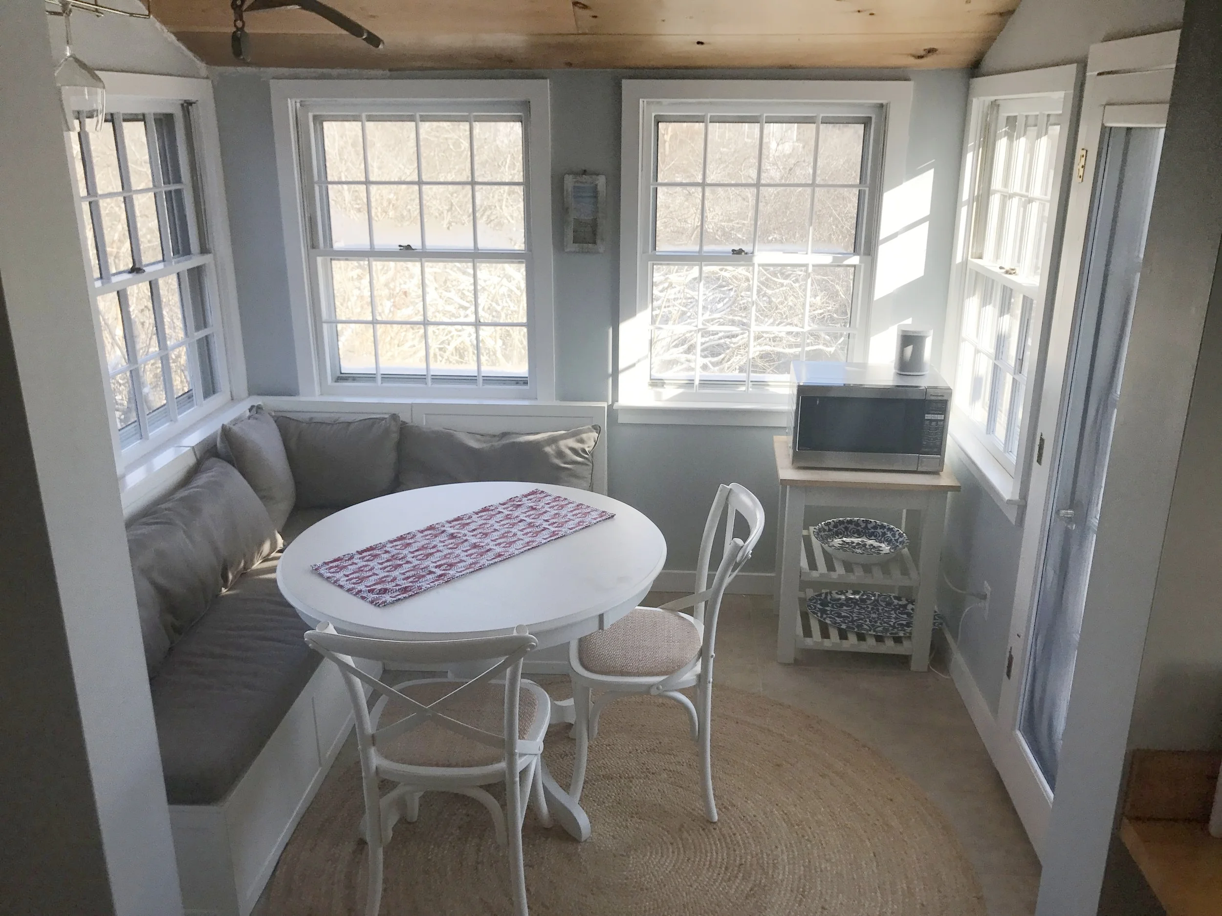 Bright dining nook with chairs and banquette seating comfortably seating 5 people.  Back door to outdoor dining table and propane grill