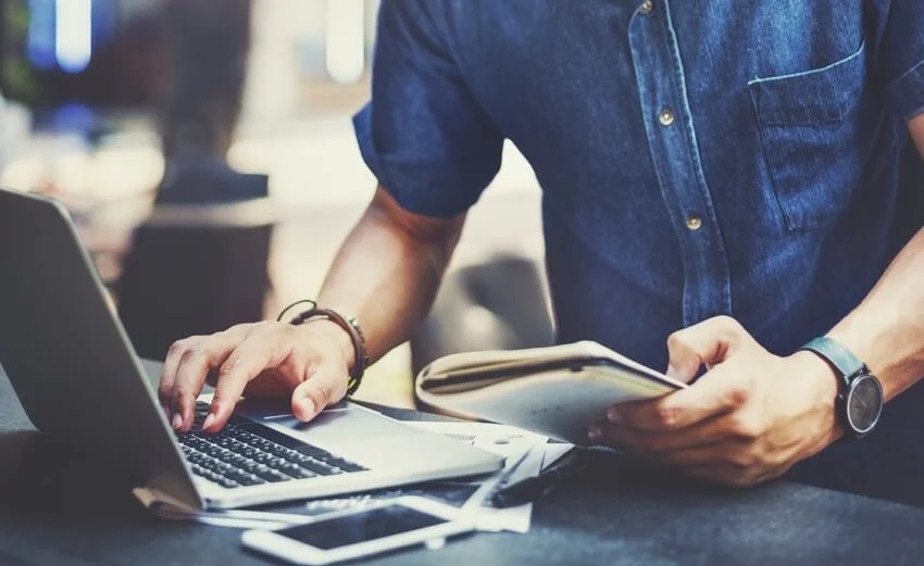 Mann an Laptop mit Unterlagen in der Hand