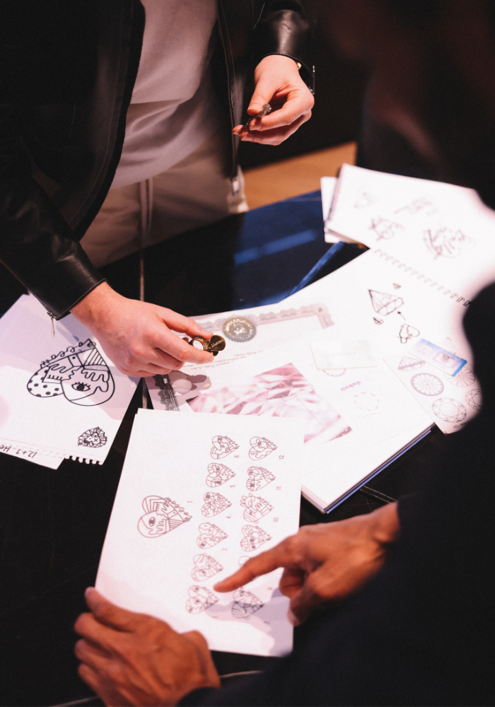 Artist Pablo Lücker studying various sketches and diagrams, including heart shapes and geometric designs, on sheets of paper spread on a table.