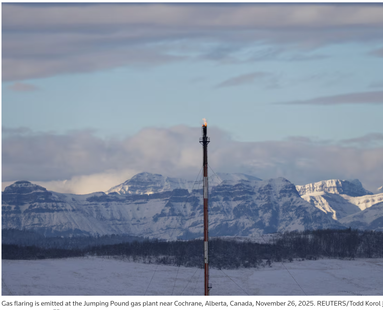 A tall, narrow smokestack with flame at the top. Behind it, snowy mountains