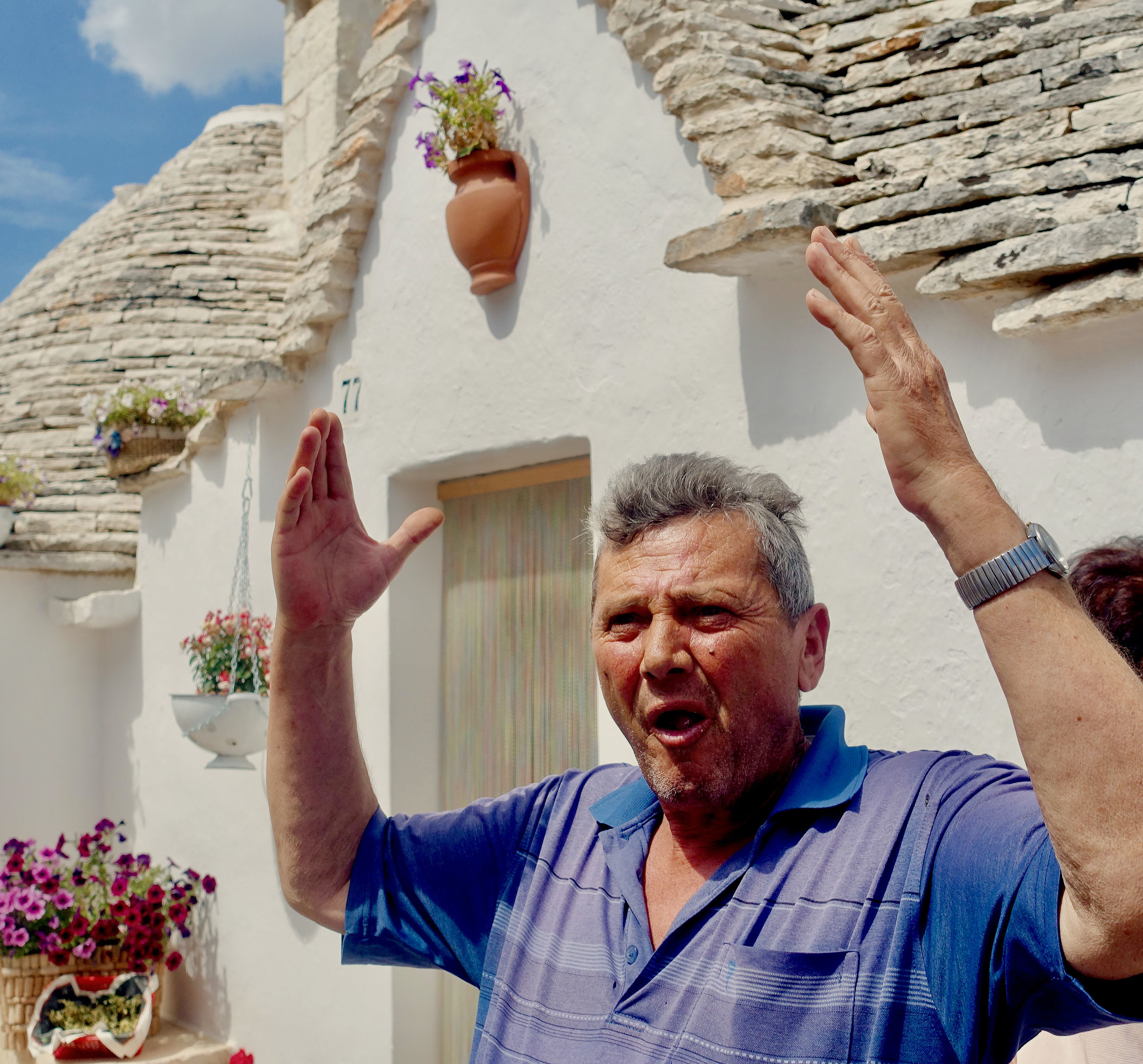  Man gestures in Alberobello, Puglia in front of his Trullo house 