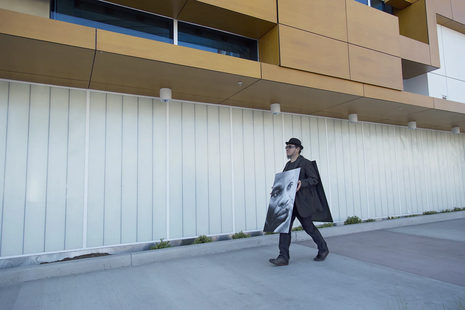100 Walkers, West Hollywood , a large scale performance piece by Richard Kraft took place on April 18th 2015. One hundred people, each dressed in a dark suit and bowler hat and wearing a sandwich board (with a unique image on both front and back) walked pre-determined routes through the city. The piece began with all one hundred walkers forming a grid in the El Tovar parking lot adjacent to West Hollywood Park. Once all one hundred walkers were in place, the maestra of ceremonies Marjorie Perloff began calling "start phrases" to release one walker at a time at approximately five second intervals. Once the walkers dispersed, they could be seen all over West Hollywood, particularly along all the main thoroughfares: Sunset, Santa Monica, Melrose, Beverly, San Vicente, Doheny, La Cienega, Crescent Heights and Fairfax. During the piece performers remained silent. Interaction with inquisitive passers by was confined to the handing out of a business card. The walk ended when all walkers returned to their starting point at the El Tovar parking lot, standing for one minute to finish their performance. For more images and further information please visit: www.onehundredwalkers.com Photo by Kyle Flath