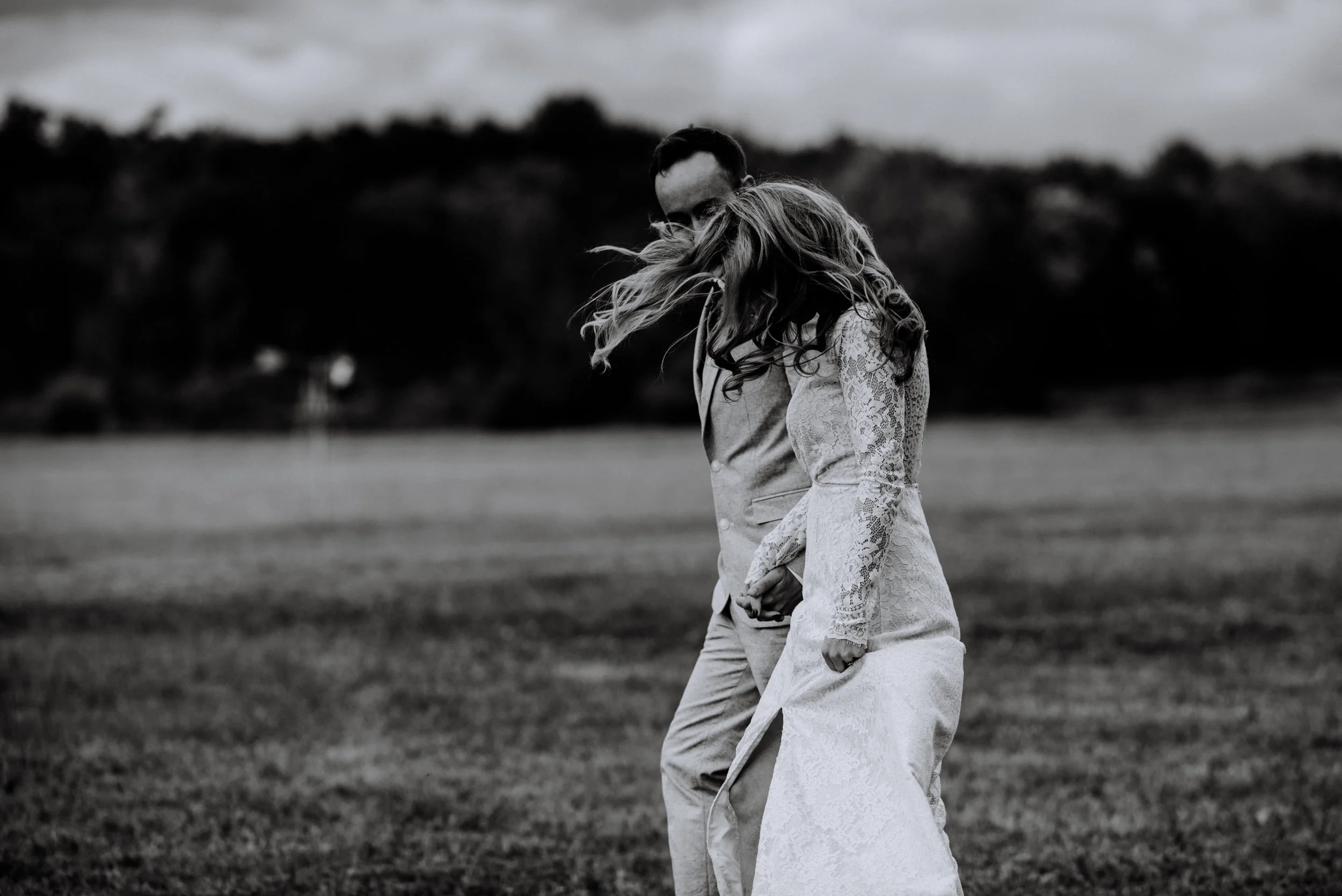 black and white candid of the wind in the bride's hair while walking hand in hand with groom