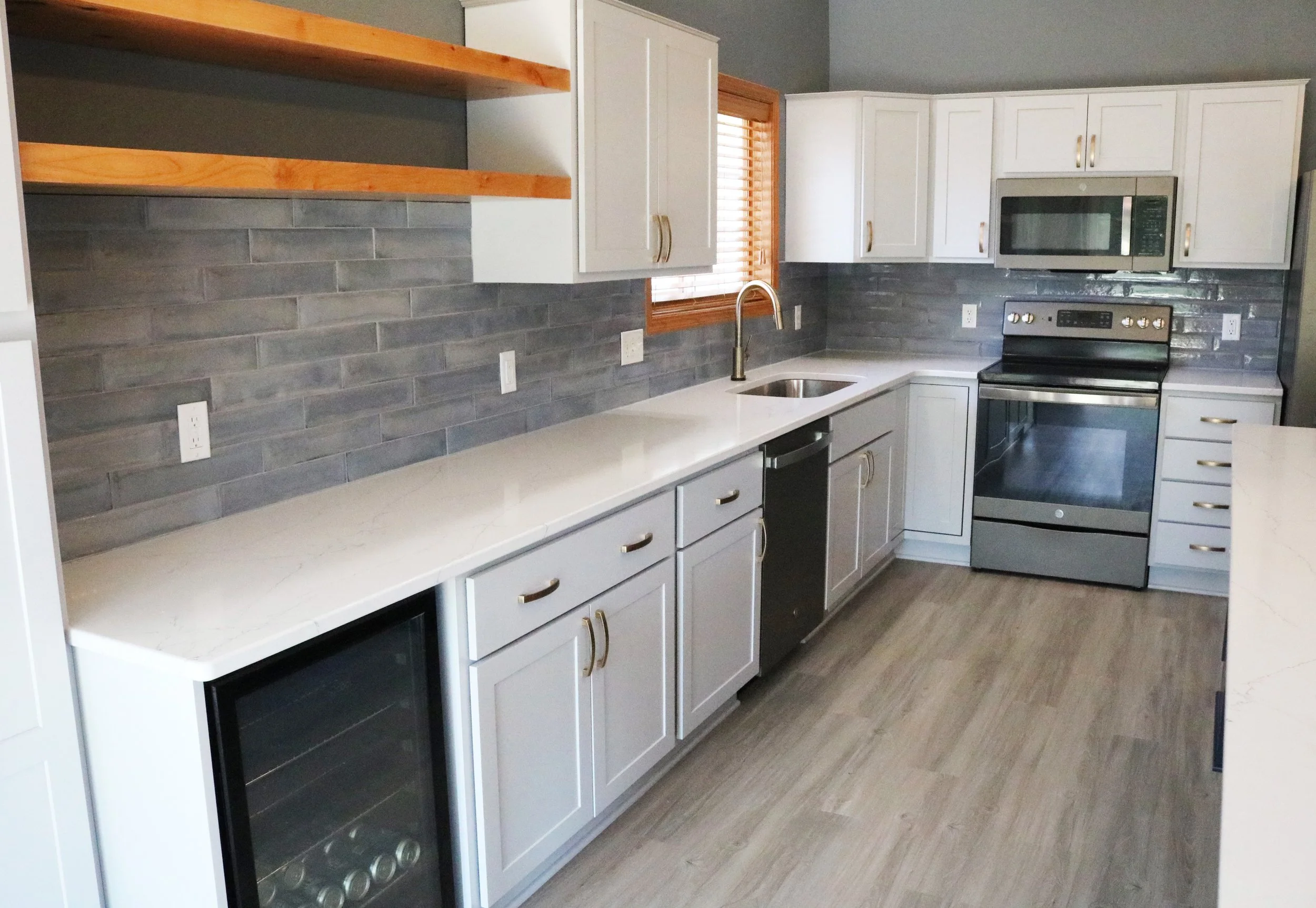 Modern kitchen with white cabinets, gray tile backsplash, stainless steel appliances, wood shelves, and light hardwood flooring.