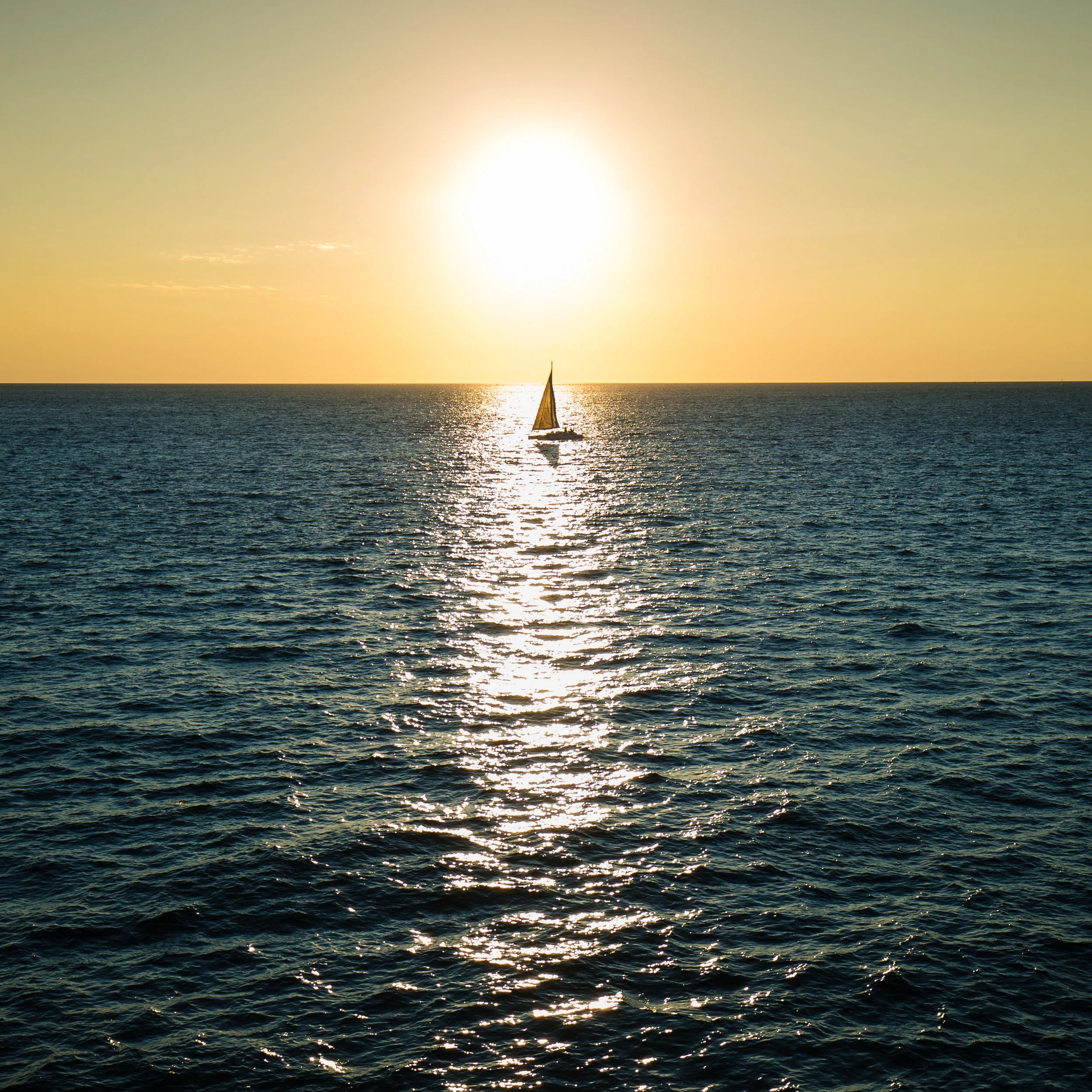 A lone sail boat crosses the early morning sun. 
