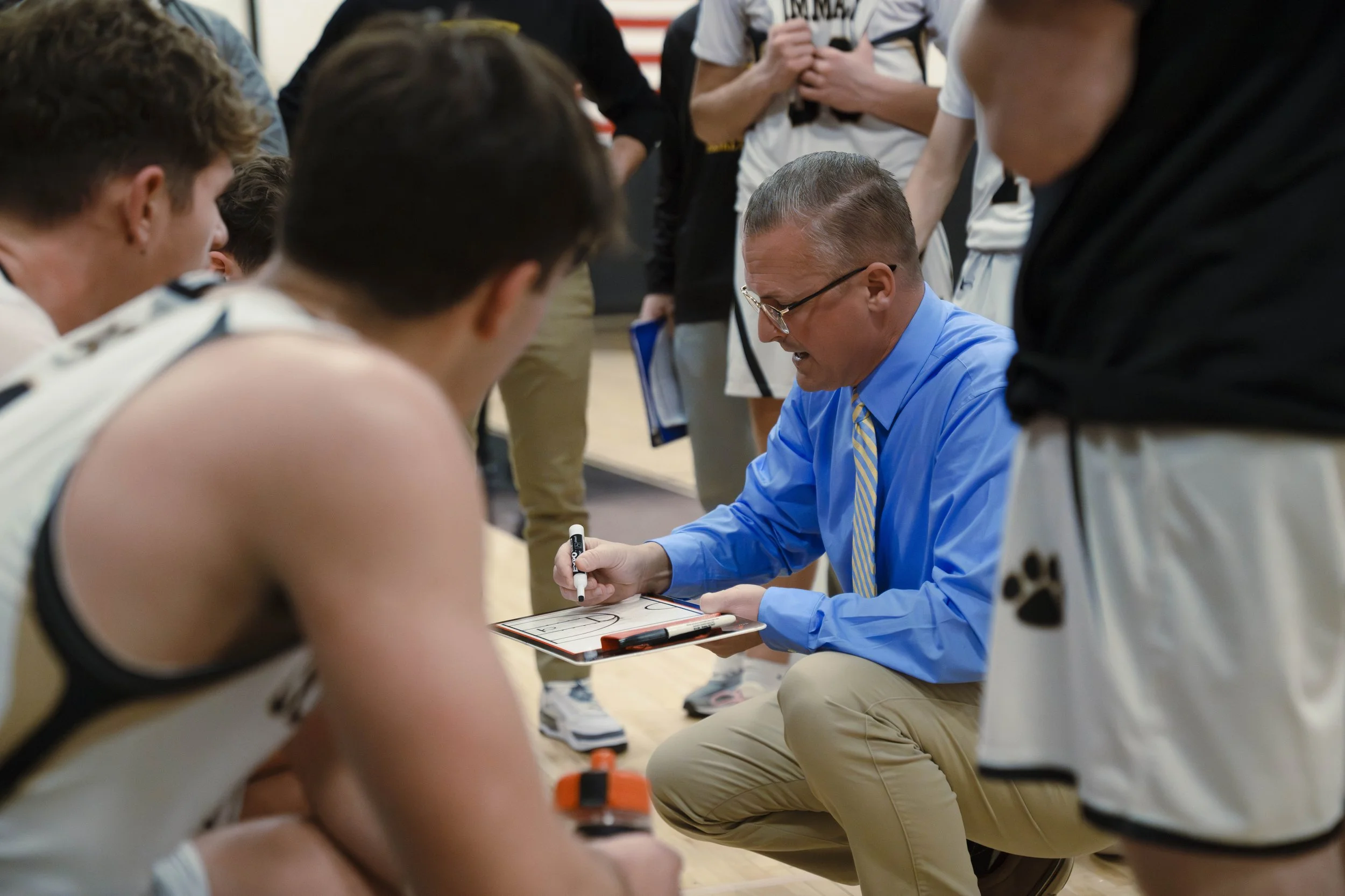 Basketball coach discussing strategy with his team during a timeout in an indoor gym.