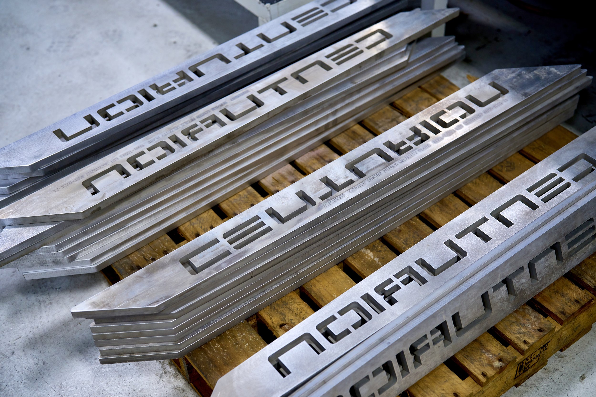 Several metal parts with cut-out text resting on a wooden pallet.