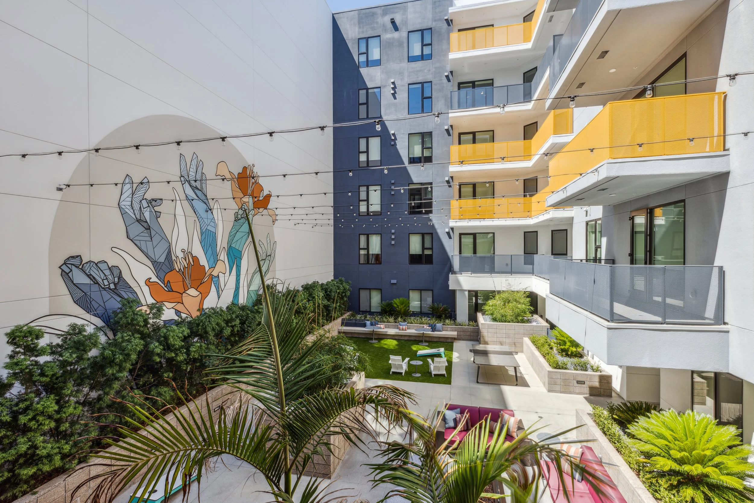 A brightly colored exterior courtyard holds a massive hand-painted mural by Allison Kunath featuring geometric hands and orange colored lilies.
