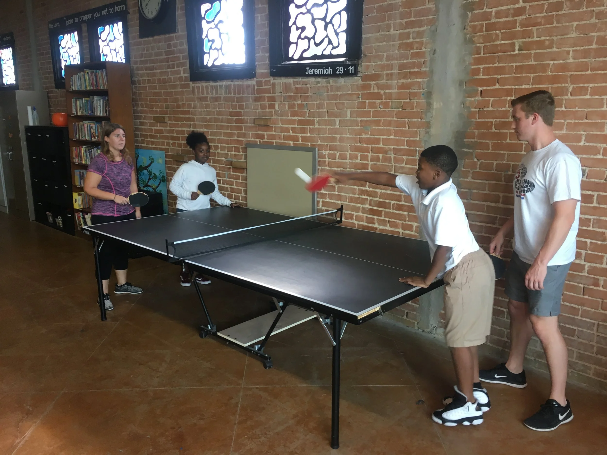 Two mentor-mentee pairs play doubles on the ping pong table.