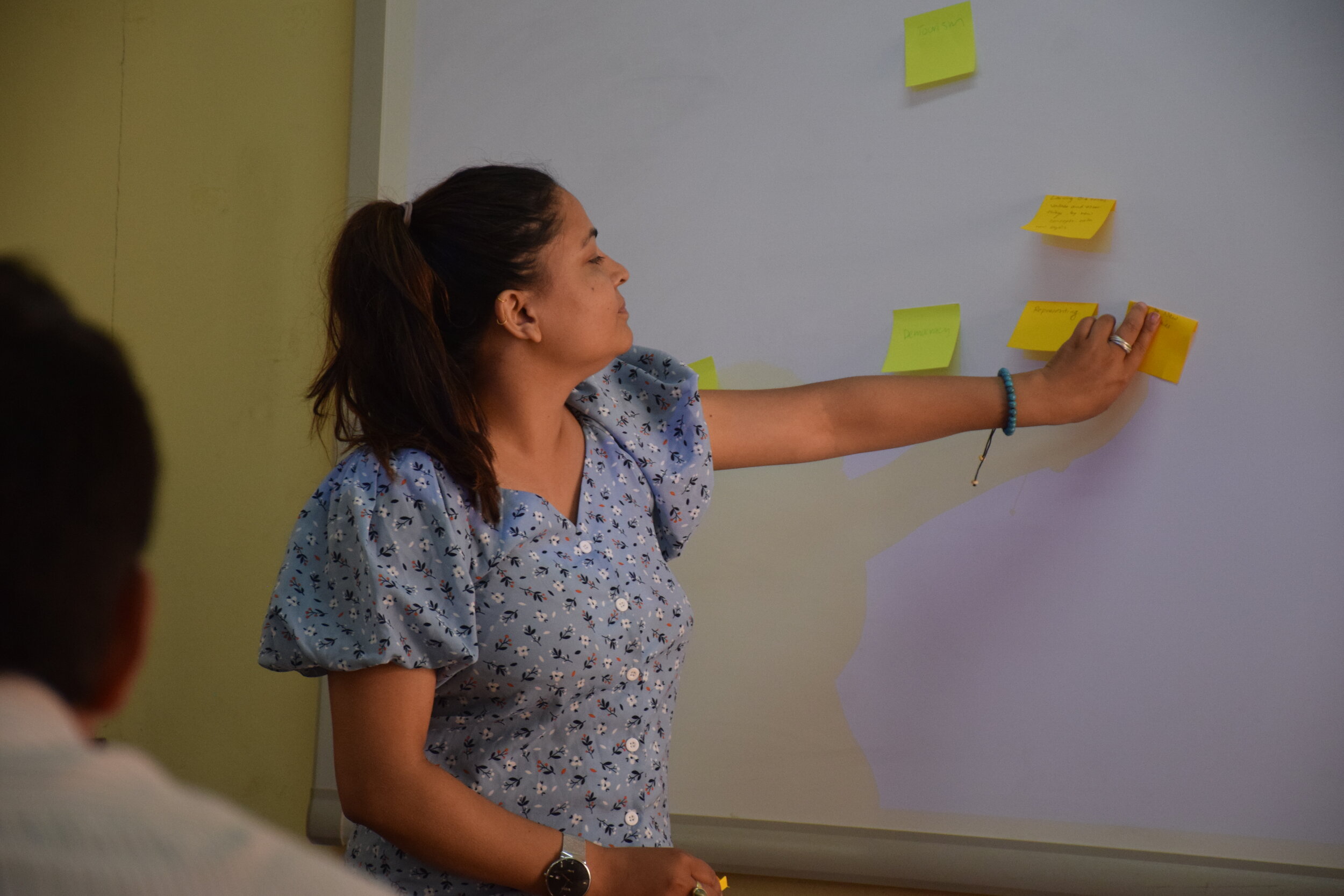 A woman arranges sticky notes on a white board