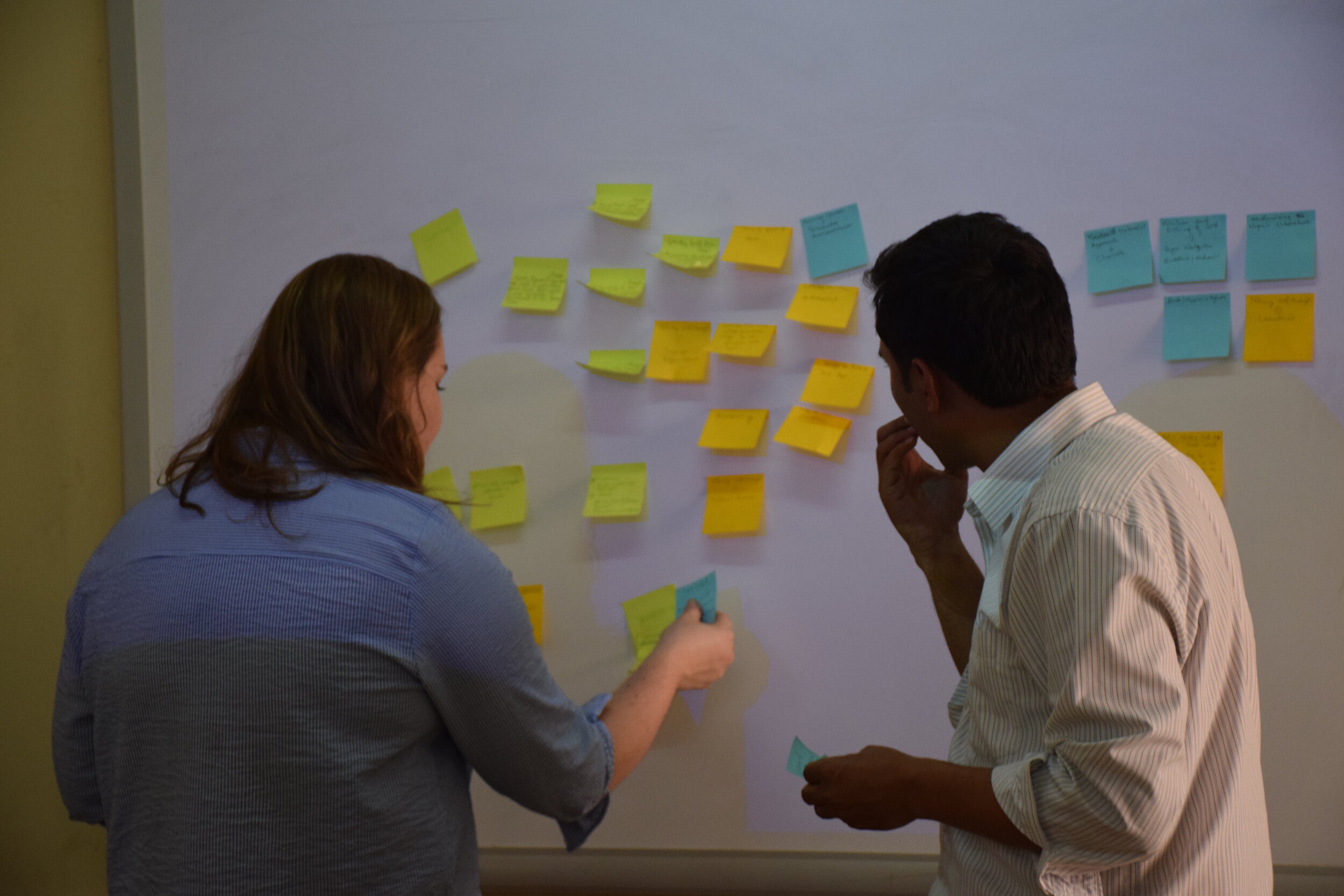 Two people arrange sticky notes on a white board during an activity. 