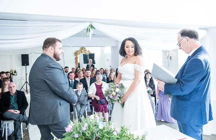Bride and groom standing hand in hand with the registrar during their wedding ceremony at Chichester Harbour Hotel.