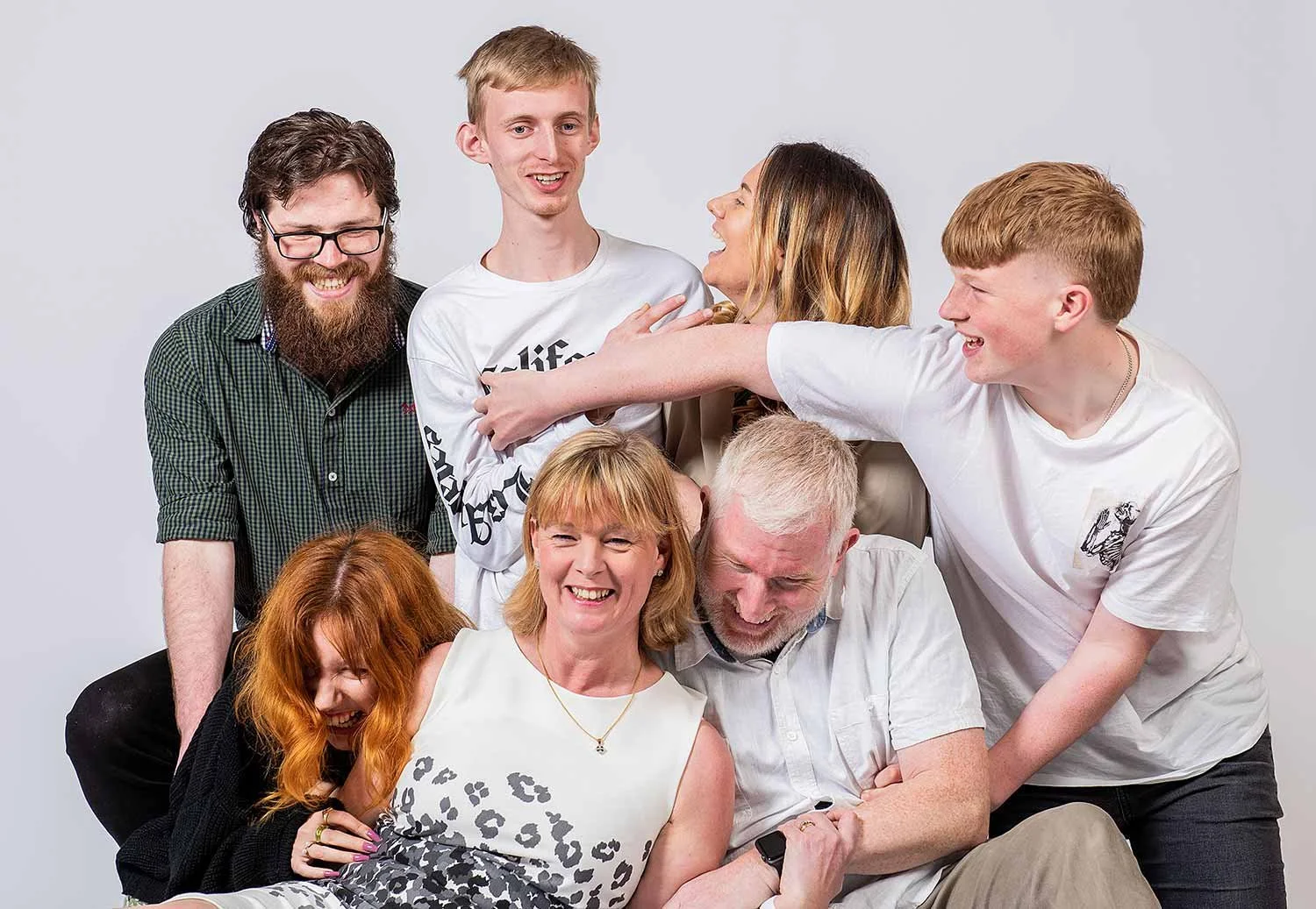 A group of seven family members enjoy a fun and playful moment during a studio photoshoot in Littlehampton, laughing and tickling each other