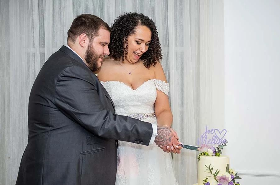 Bride and groom cutting their wedding cake at Chichester Harbour Hotel in Chichester, West Sussex, surrounded by guests.
