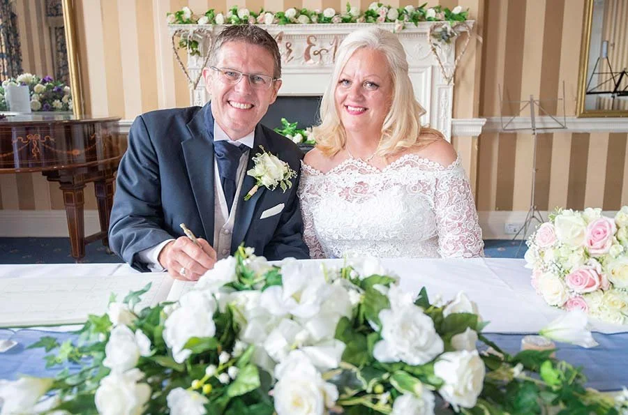 Bride and groom smiling while signing the marriage register at The Norfolk Arms in Arundel, West Sussex.
