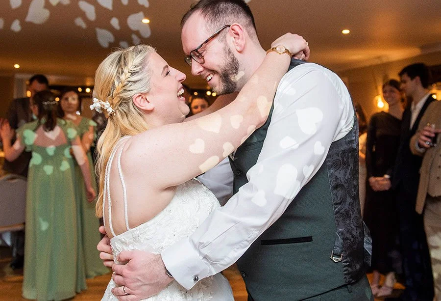 Newlyweds dancing their first dance in a warmly lit reception hall surrounded by guests.