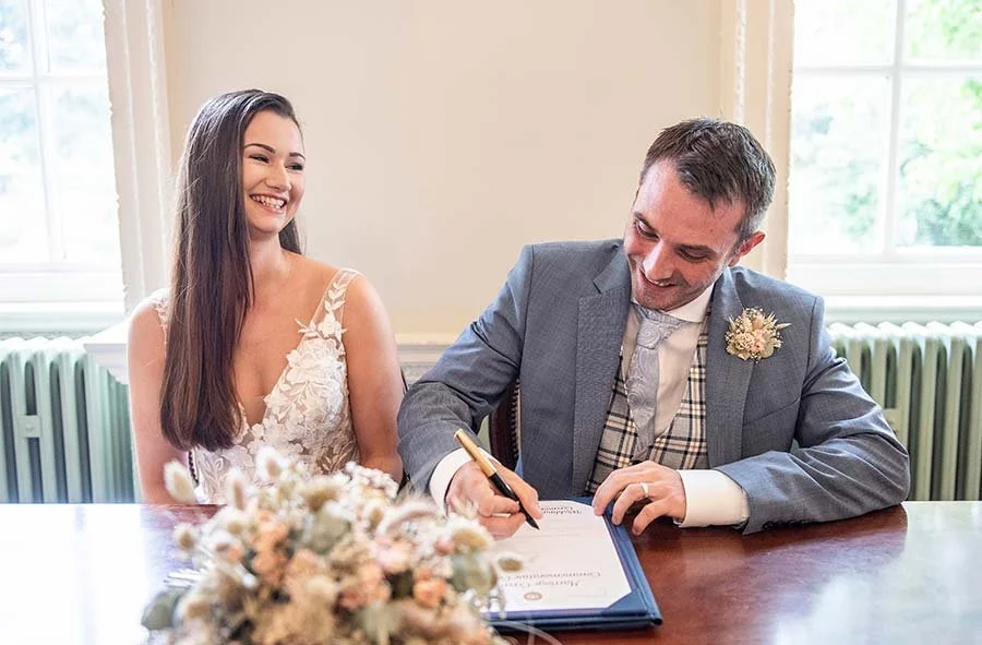 Bride and groom laughing while signing the marriage register at Park House Registry Office in Horsham, West Sussex.