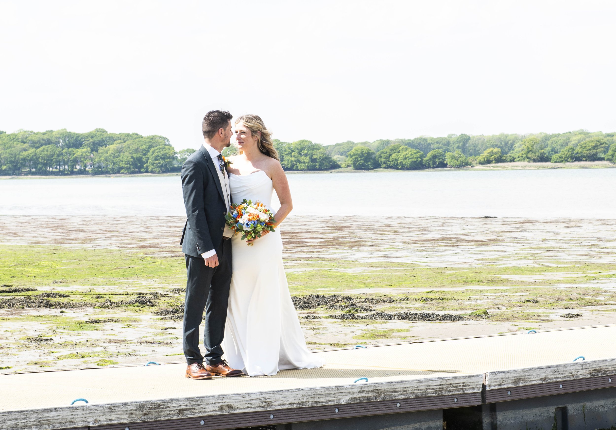 becca and oz standing near water for their wedding photos