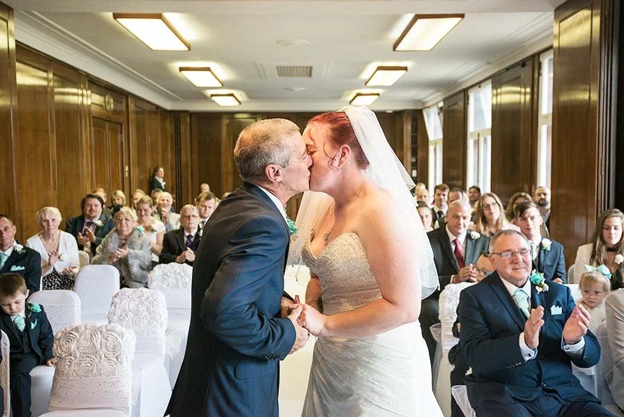 Bride and groom holding hands and kiss inside Worthing Town Hall during their civil ceremony.