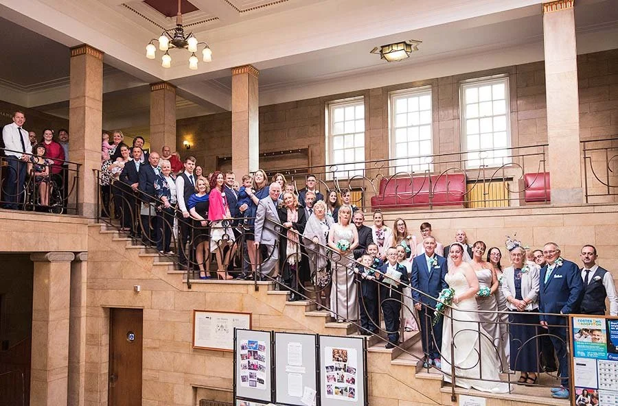 Large group wedding photo with bride, groom, and guests inside Worthing Town Hall.