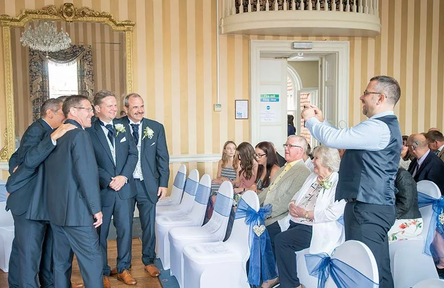 Groomsmen group photo at The Norfolk Arms in Arundel, West Sussex, with guests taking photos and laughing during the wedding celebrations.