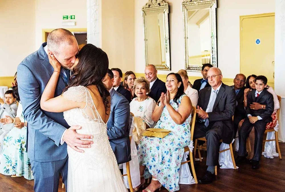 Bride and groom kissing during ceremony while guests cheering at Worthing Dome, Worthing.