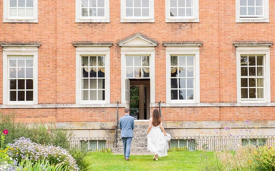 Bride and groom walking back inside Park House Registry Office in Horsham, West Sussex, after their ceremony, sharing a joyful moment.